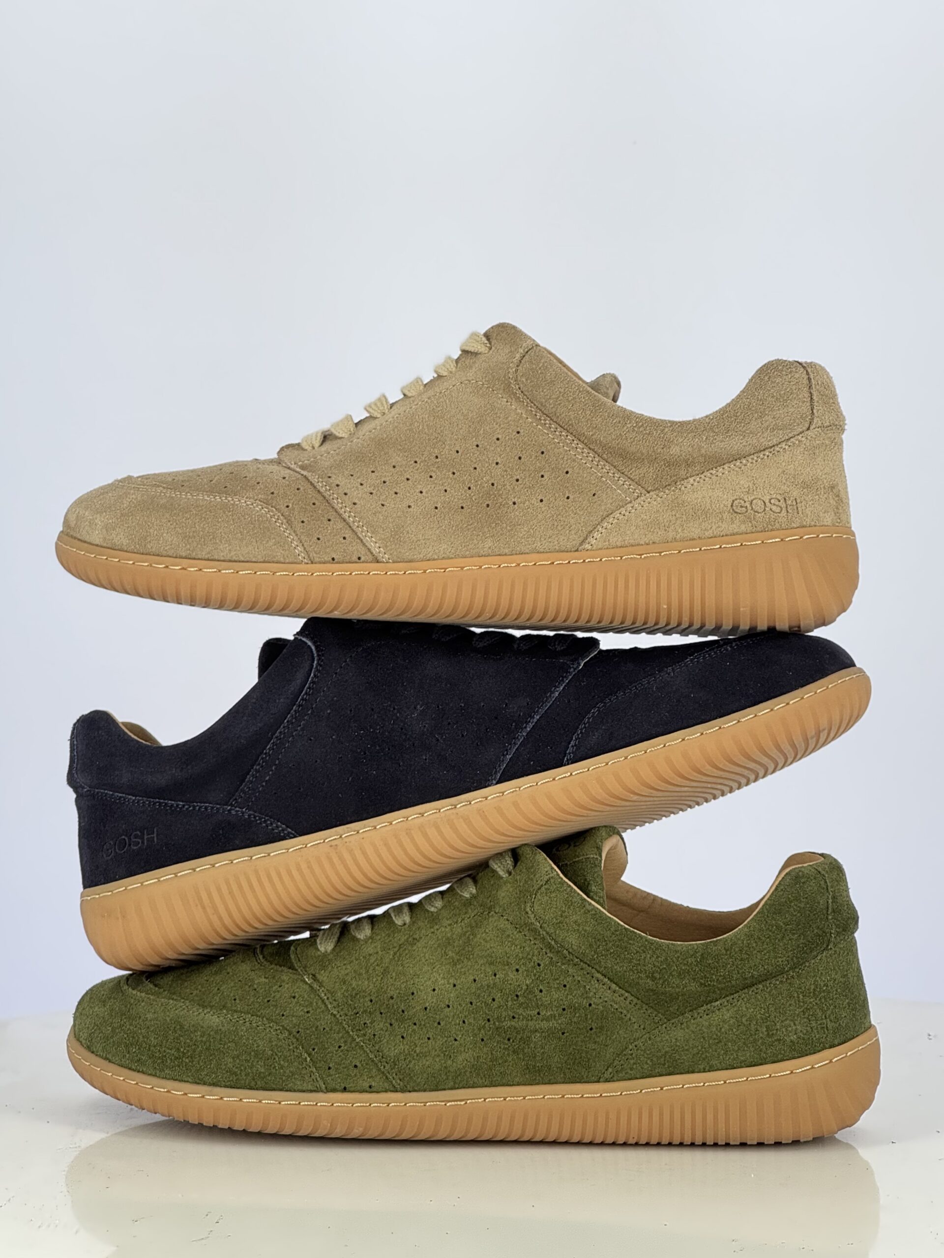 Three suede sneakers in beige, blue, and green stacked together
